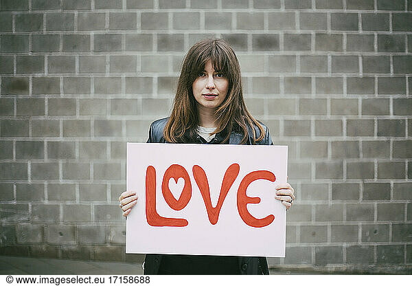 Portrait of female activist with love poster against wall