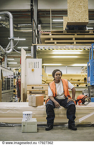 Portrait of female blue-collar worker sitting by hardhat in warehouse