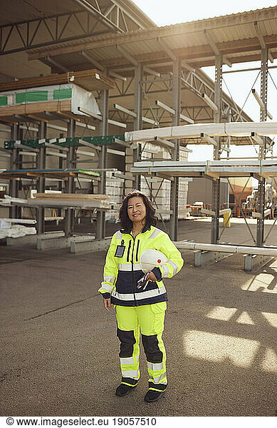 Portrait of female blue-collar worker with hardhat standing outside industry