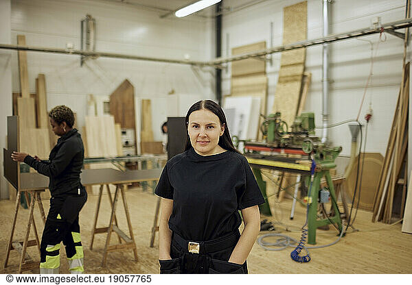 Portrait of female carpenter standing with hands in pockets at workshop