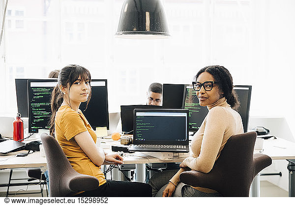 Portrait of female computer hackers sitting desk in creative office