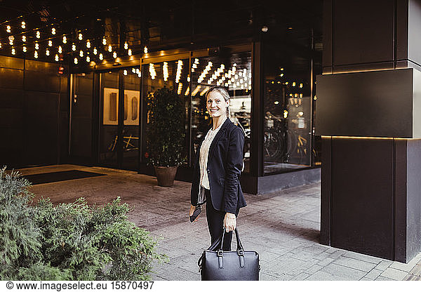 Portrait of female entrepreneur with bag standing at building entrance