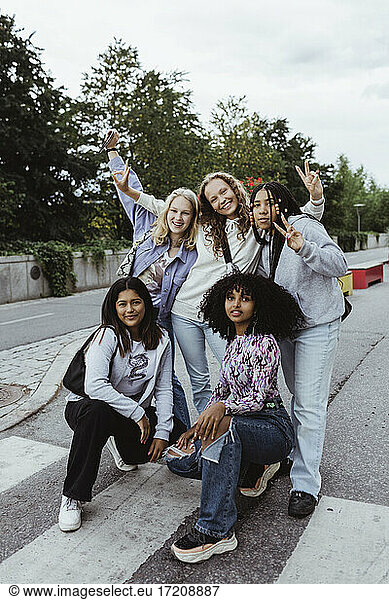 Portrait of female friends gesturing with peace sign on street