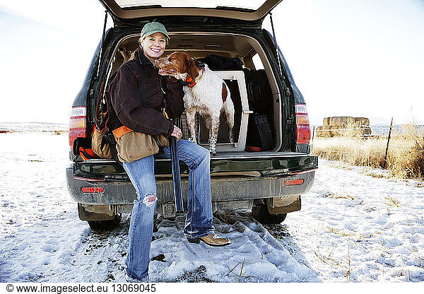 Portrait of female hunter sitting with dog in car trunk