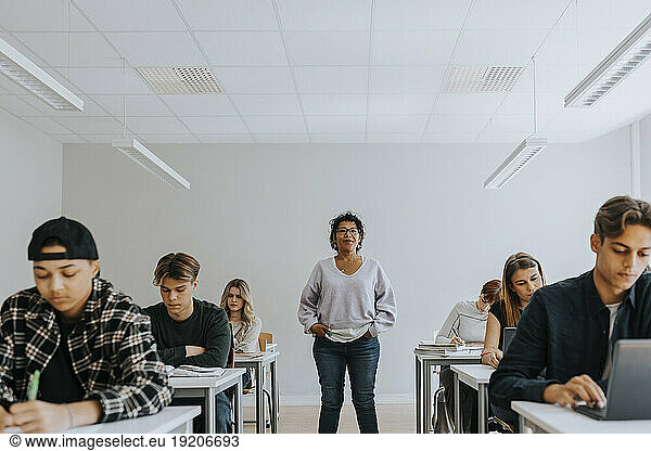 Portrait of female teacher with hands in pockets standing amidst students