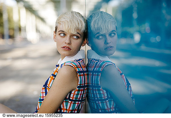 Portrait of female teenager wearing colorful dress mirrored in glass pane