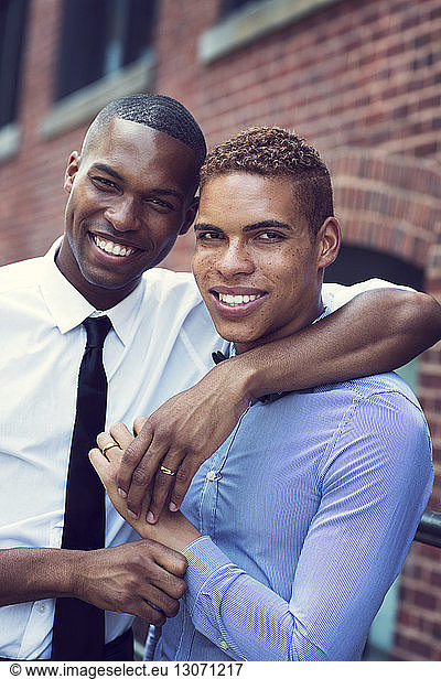 Portrait of gay couple with arm around standing against building in city