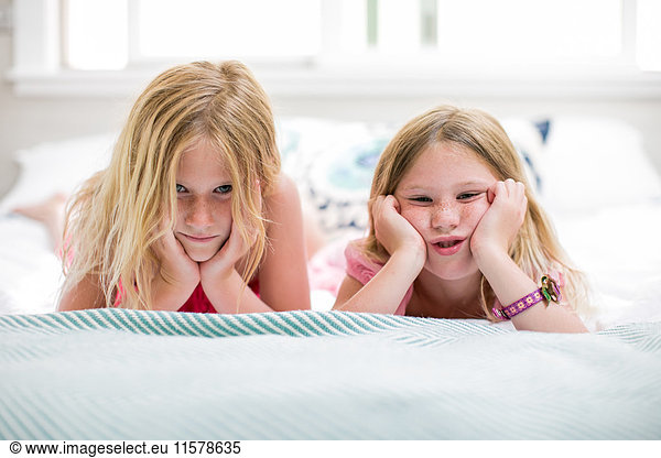 Portrait of girl and sister pulling faces on bed
