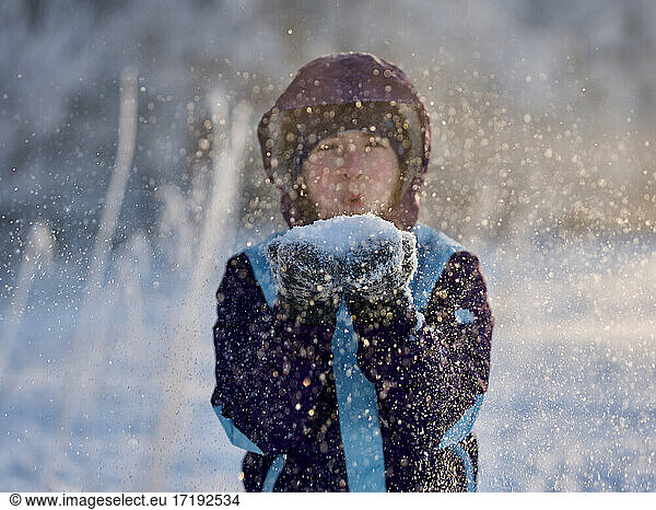 Portrait of girl blowing snowflakes to camera in winter  focus on snow