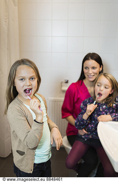 Portrait of girl brushing teeth with mother and daughter in bathroom