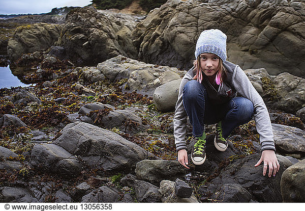 Portrait of girl crouching on rocks at beach