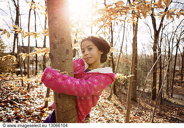 Portrait of girl embracing tree trunk during autumn