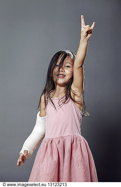 Portrait of girl gesturing hand sign against gray background