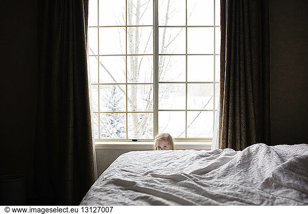 Portrait of girl hiding behind bed at home