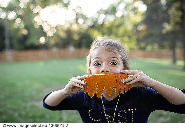 Portrait of girl holding carved pumpkin while standing in yard during Halloween