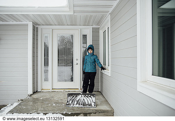 Portrait of girl in warm clothing standing at entrance by house