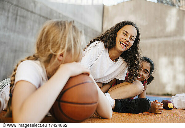 Portrait of girl laughing while sitting with female friends at basketball court
