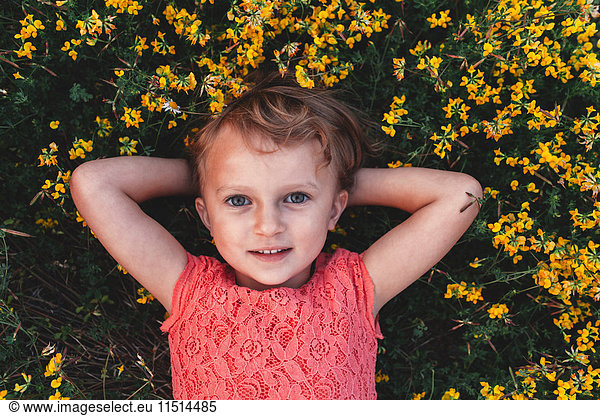Portrait of girl lying on back amongst yellow wildflowers