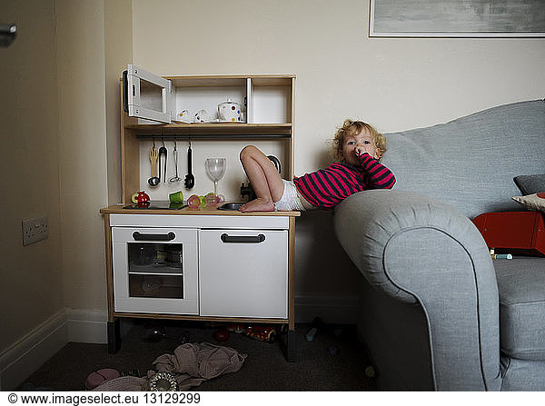 Portrait of girl lying on sofa and toy kitchen counter