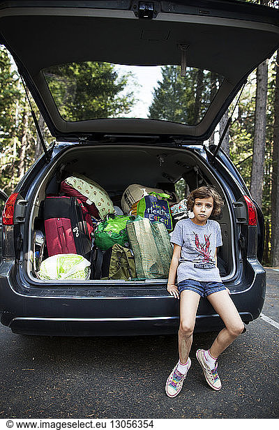 Portrait of girl sitting on car trunk at road