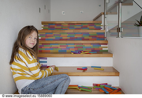 Portrait of girl sitting on stairs and playing with wooden blocks