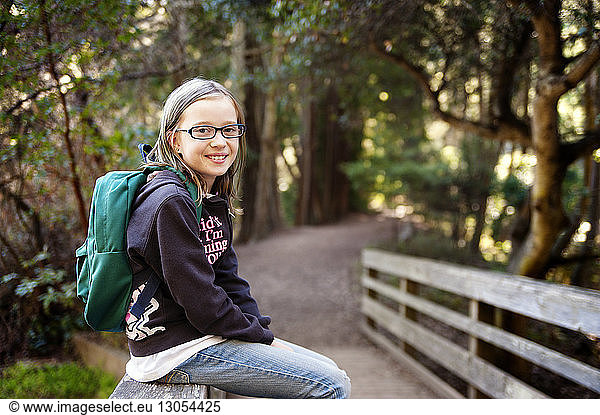 Portrait of girl with backpack sitting on railing