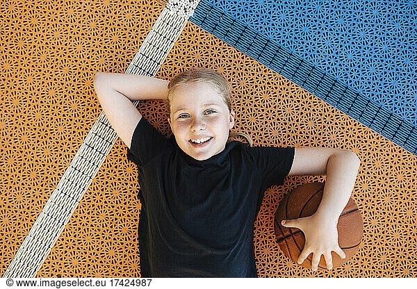 Portrait of girl with basketball lying down at sports court