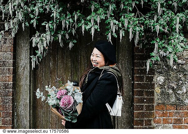 portrait of happy Asian woman stood in English doorway with flowers