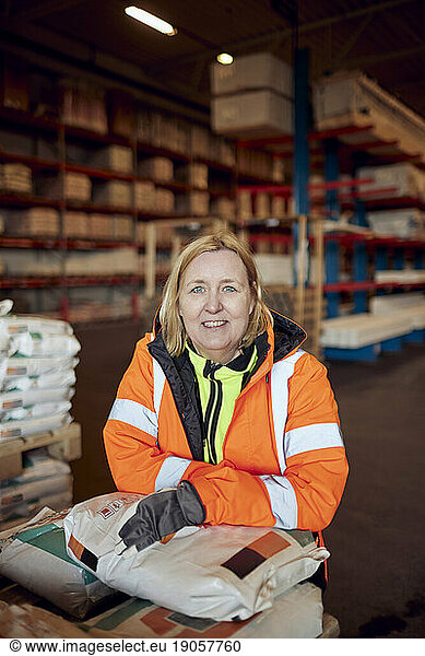 Portrait of happy blue-collar worker in protective workwear leaning on package in distribution warehouse