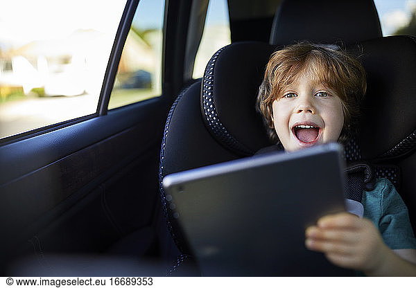 Portrait of happy boy using tablet PC while sitting at back seat in car