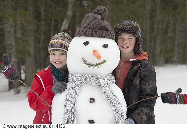 Portrait of happy boys posing with snowman