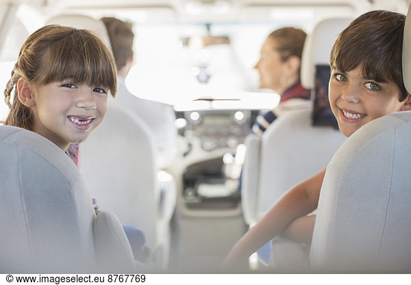 Portrait of happy brother and sister in back seat of car