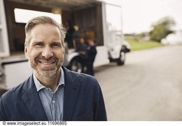 Portrait of happy businessman standing on road with colleagues and portable office truck in background