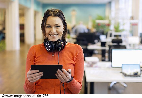 Portrait of happy businesswoman holding digital tablet in creative office