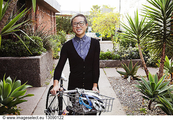 Portrait of happy businesswoman with bicycle standing at park
