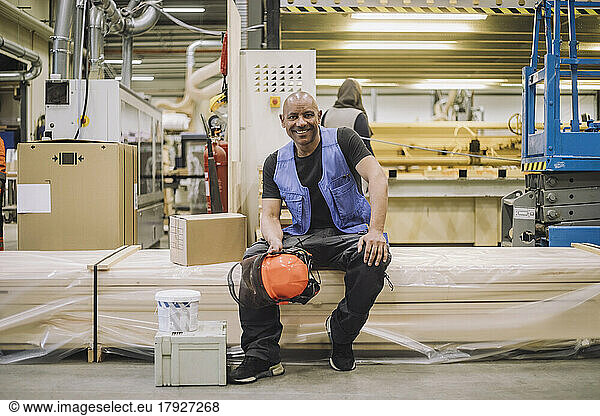 Portrait of happy carpenter sitting with hardhat in warehouse