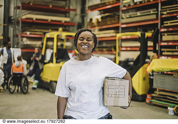Portrait of happy carpenter with cardboard box at warehouse