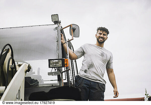 Portrait of happy construction worker standing at doorway of vehicle