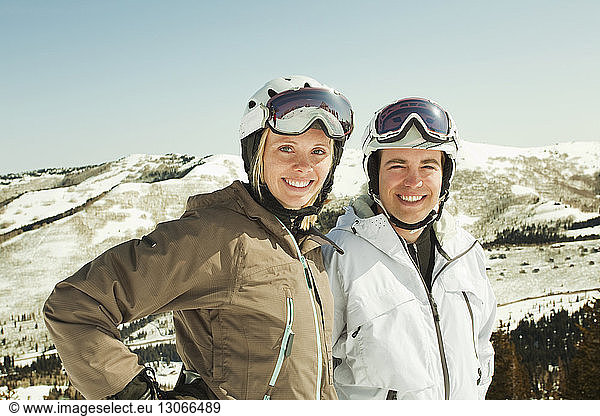 Portrait of happy couple in ski-wear standing against snowcapped mountain