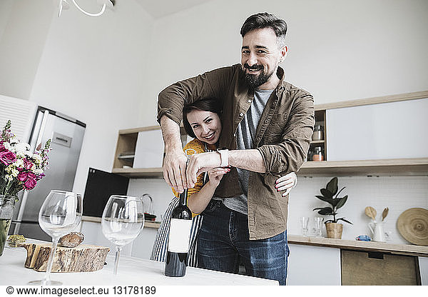 Portrait of happy couple with bottle of red wine in the kitchen