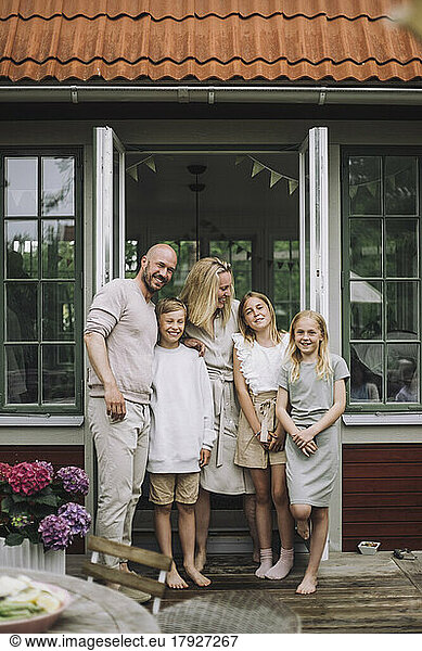 Portrait of happy family standing together against doorway on porch