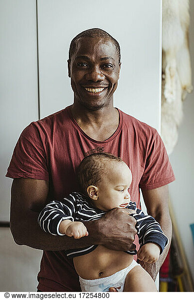 Portrait of happy father carrying toddler son at home