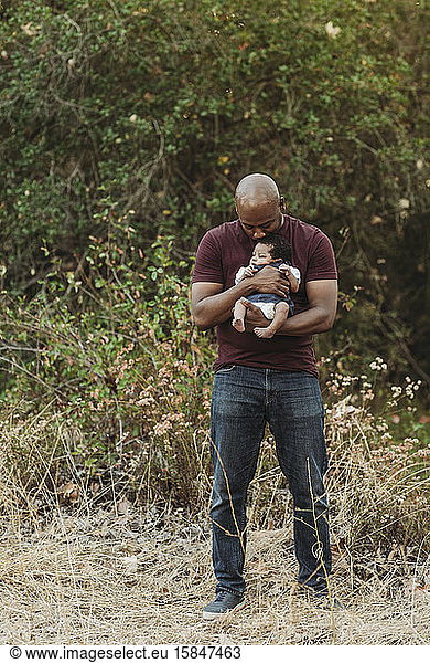 Portrait of happy father holding newborn age daughter in backlit field