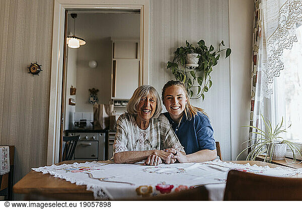 Portrait of happy female caregiver with senior woman sitting at home