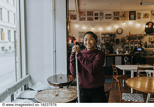 Portrait of happy female owner standing by table in coffee shop