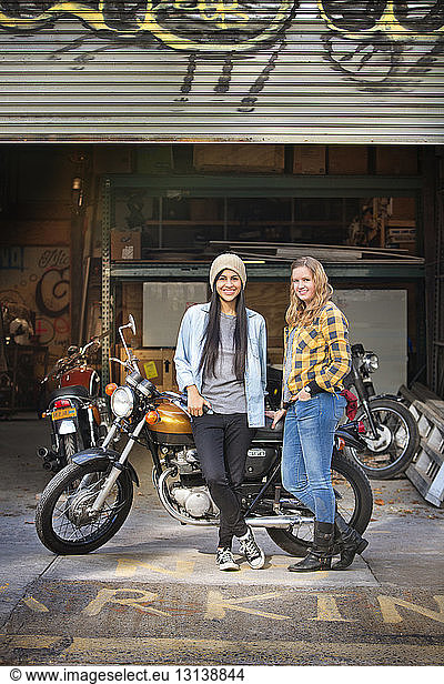 Portrait of happy female owners standing with bike outside auto repair shop