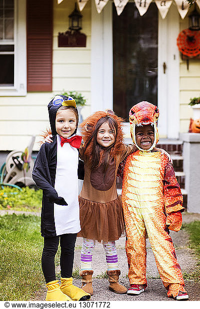Portrait of happy friends in Halloween costume standing against house