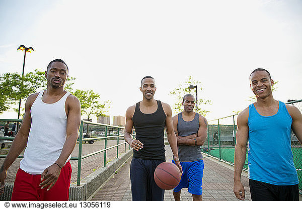 Portrait of happy friends with basketball walking on footpath in park