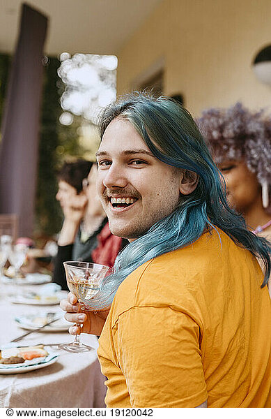 Portrait of happy gay man with dyed hair enjoying with friends during dinner party in back yard