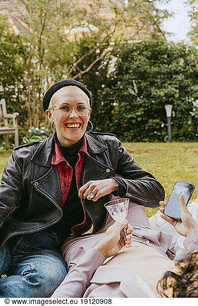 Portrait of happy gay woman wearing leather jacket while sitting with friend in back yard